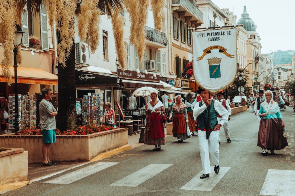 People in traditional clothing parade through a Cannes street during a vibrant festival.